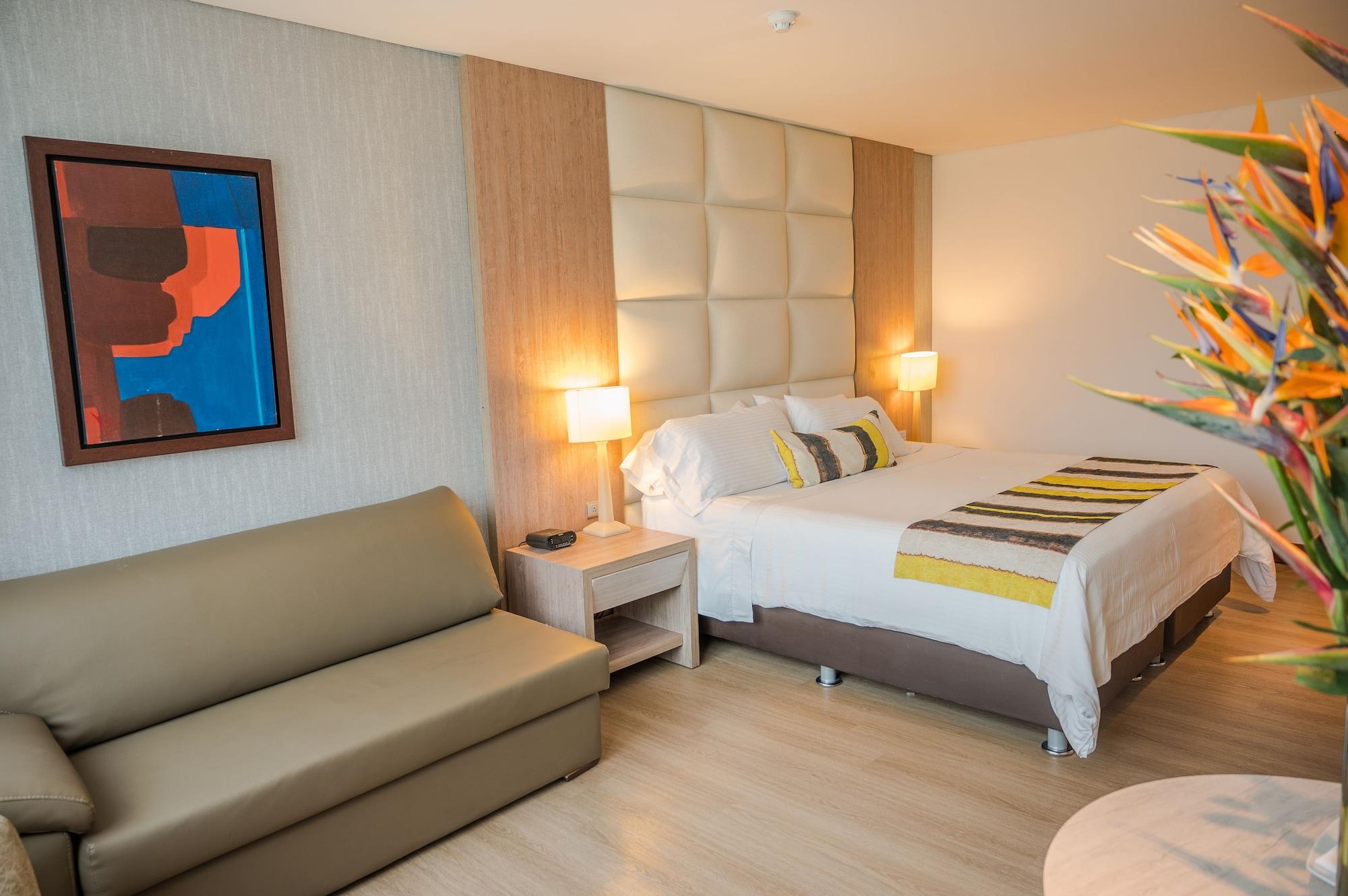 Hotel San Fernando Plaza Medellín Esterno foto The photo shows a stylish hotel room. It features a comfortable bed with decorative pillows and a striped blanket. On either side of the bed, there are bedside lamps providing warm lighting. There is a modern artwork framed on the wall next to the be